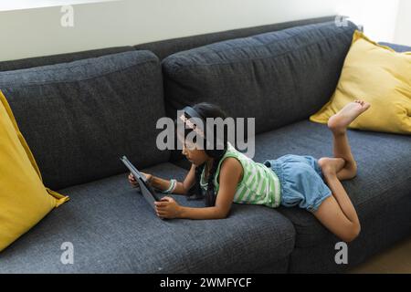 Biracial Girl liegt auf einer Couch mit einem Tablet zu Hause mit Kopierraum Stockfoto