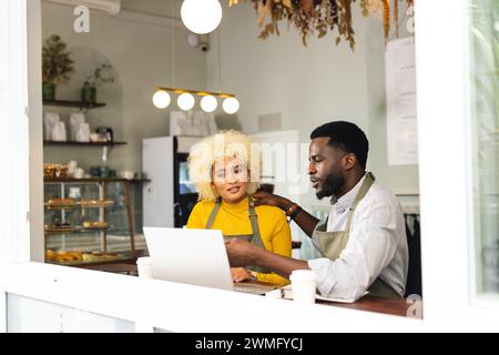 Ein afroamerikanischer Mann hilft birassischen Frauen in einem Café, mit Kopierraum Stockfoto