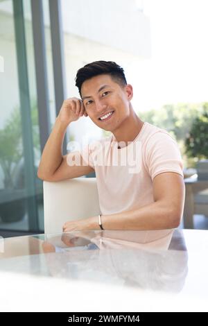 Ein junger asiatischer Mann lächelt, während er an einem Tisch sitzt Stockfoto