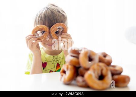 Süßes Schulkind, Junge, der Donuts zu Hause isst, hausgemachte frische Donuts mit Zucker bestreut Stockfoto