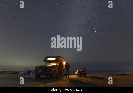 Ein Mann, der die Sterne neben dem Wohnmobil vor dem Meer ansieht Stockfoto