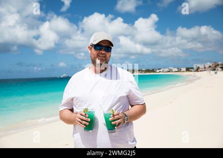 Millennial man in hat hält zwei Blue Drinks am Caribbean Beach Stockfoto