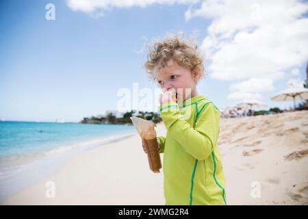 Ein Kleinkind mit lockigen Haaren isst Cracker von Package, während er in der Karibik ist Stockfoto