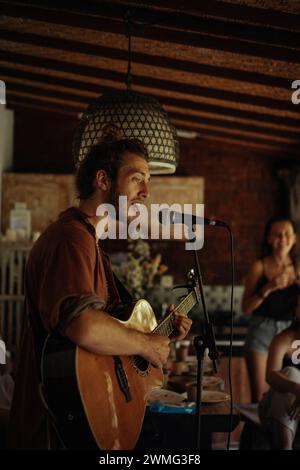 Ein junger Musiker spielt Gitarre und singt in ein Mikrofon. Stockfoto
