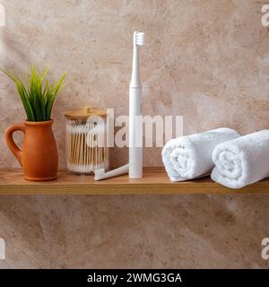 Eine elektrische Zahnbürste und weiße Handtücher auf einem Regal im Bad Stockfoto