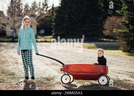 Vollständige Ansicht eines jungen Mädchens, das lächelt, während er den Jungen in einem Spielzeugwagen zieht Stockfoto