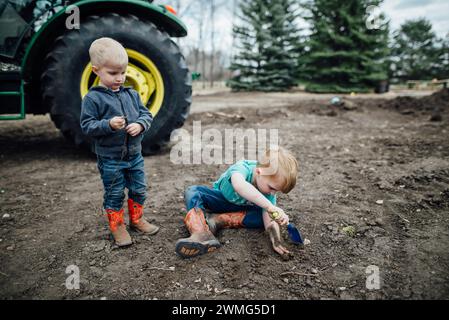 Vorderansicht von zwei Jungen, die mit einer Schaufel auf dem Schotterhof spielen Stockfoto