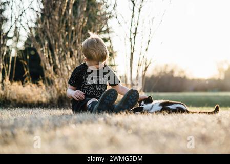 Niedrige Vorderansicht eines Jungen, der auf Gras sitzt und eine glückliche Katze streichelt Stockfoto