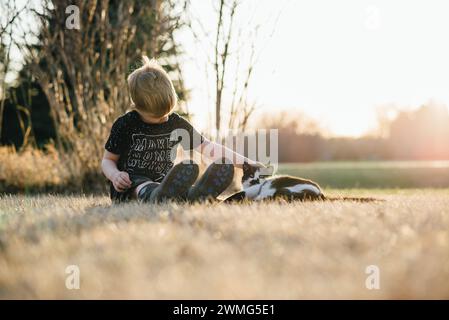 Niedrige Vorderansicht eines Jungen, der auf dem Boden neben einer glücklichen Katze sitzt Stockfoto