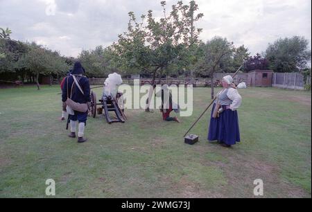 Eine dickköpfige Frau entspannt ihren Stab-Pike, um andere Mitglieder der Sealed Knot Society aus dem 17. Jahrhundert zu beaufsichtigen, die in englischer Bürgerkriegskostüme verkleidet sind, feuern eine Kanjon ab, während sie vor Gästen im Außenbereich des National Trust auftreten, The Fleece Inn, Bretforton, Worcestershire, an einem Septembertag, an dem die Sealed Knot Society eine Nachstellung des 17. englischen Bürgerkriegs gab Stockfoto