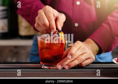 Nahaufnahme der Hände eines Barkepers, die einem gekühlten Cocktailglas eine Zitrusgarnitur hinzufügen Stockfoto