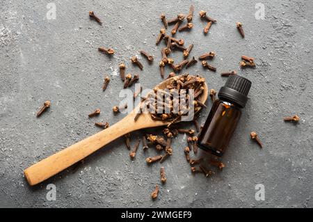 Schließen Sie eine Glasflasche mit ätherischem Nelkenöl und Nelken in Holzlöffel auf rustikalem Hintergrund. Kräuter- und Gewürzöl-Konzept Stockfoto