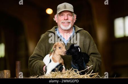 Schneverdingen, Deutschland. Februar 2024. Uwe Storm, Hirte, hält ein nur wenige Tage altes Ziegenlamm (l) und ein Schnuckenlamm (r). Die Lammsaison ist der Beginn der geschäftigsten Zeit des Jahres für die Heide-Hirten. Quelle: Philipp Schulze/dpa/Alamy Live News Stockfoto