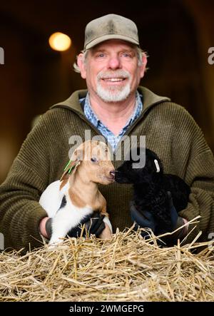 Schneverdingen, Deutschland. Februar 2024. Uwe Storm, Hirte, hält ein nur wenige Tage altes Ziegenlamm (l) und ein Schnuckenlamm (r). Die Lammsaison ist der Beginn der geschäftigsten Zeit des Jahres für die Heide-Hirten. Quelle: Philipp Schulze/dpa/Alamy Live News Stockfoto