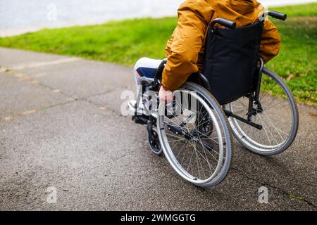 Nahaufnahme eines Querschnittsgelähmten behinderten Mannes im Rollstuhl im Park. Er rollt auf dem Weg. Stockfoto