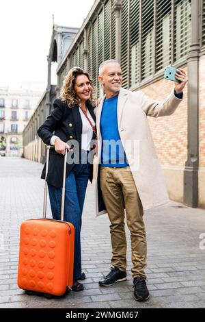 Glückliches Touristenpaar im mittleren Erwachsenenalter, das zusammen reist und ein Selfie mit ihrem Gepäck macht. Liebevoller älterer Ehemann und Ehefrau, die während eines Fotos machen Stockfoto