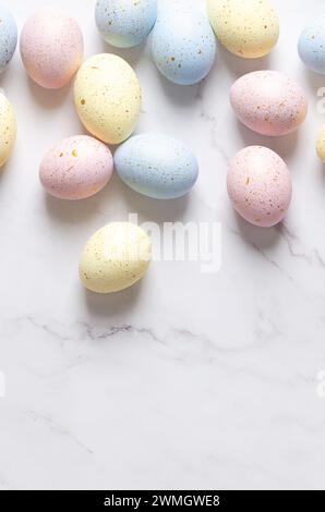 Osterhintergrund mit pastellfarbenen Eiern mit goldenen Flecken auf einem weißen Marmortisch. Vertikales Format und Kopierraum. Stockfoto