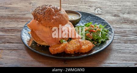 Teller mit Lachsburger und Rosti auf strukturiertem Holztisch Stockfoto