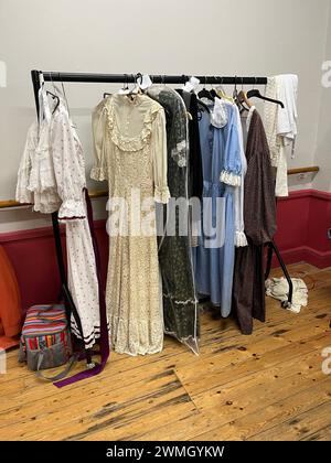 Theaterkostüme hängen hinter der Bühne im Theater an einem Schienen. Kleider im Vintage-Stil in Creme, weiß, Blau und Braun. Stockfoto