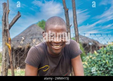 Glückliche afrikanische Männer, mit einem zahnigen Lächeln, stehen vor einer strohgedeckten Hütte. Stockfoto