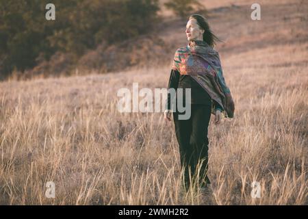 Porträt einer erwachsenen Kaukasierin mit einem zurückhaltenden Lächeln im Sonnenuntergang in einer Herbstlandschaft. Vertikale Zusammensetzung. Stockfoto