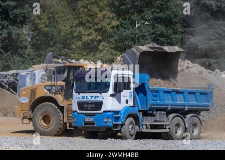 Nancy, Frankreich – Schwerpunkt auf einem gelben Radlader CAT 966H, der einen Kipplader MAN TGS 26,400 für Erdarbeiten auf einer Baustelle beladen soll. Stockfoto