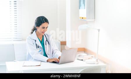 Schöne und professionelle Ärztin, die einen Laptop benutzt und an ihrem Schreibtisch in der Arztpraxis arbeitet. Stockfoto