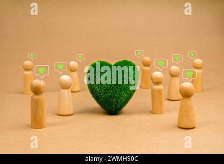 Grünes Herz in der Mitte der Gemeindegruppe Holzfiguren mit grünem Herz, Liebessymbol in der Sprechblase stehen auf recyceltem Papier Hintergrund. Eart Stockfoto