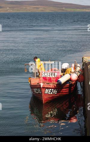 Ein kleines Fischerboot mit einem Fischer an Bord, das neben dem Tingwall Pier, Orkney, Schottland, Großbritannien, vor Anker liegt Stockfoto