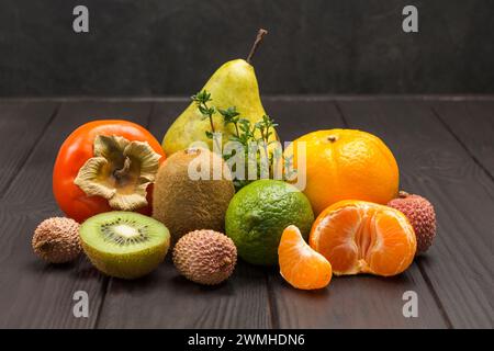 Verschiedene exotische Früchte in verschiedenen Farben. Mandarinen und Orangen, Kiwi und Birne, Persimmon und Litschi. Kopierbereich. Dunkler Holzhintergrund Stockfoto