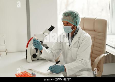 Männlicher Wissenschaftler, der Notizen in einem Notizblock macht, während er Tests in einem Forschungslabor durchführt Stockfoto