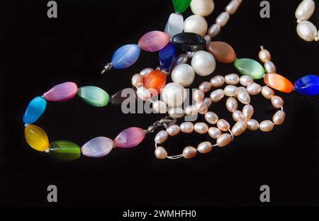 Farbige Steine und eine Kette von Perlen (verschiedene Größen weiß und rosa Farbe), hergestellt in Indien auf schwarzem Stoff - atemberaubende Erinnerungen an den großen Südstaaten-Staat Stockfoto