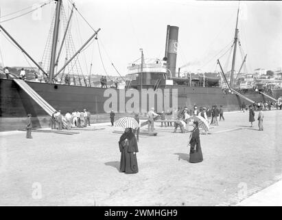 Eine Gruppe von Männern und Frauen läuft neben einem großen Schiff in einem Südosthafen. Anfang des 20. Jahrhunderts. Altes Foto digitalisiert von Glasplatte. Stockfoto
