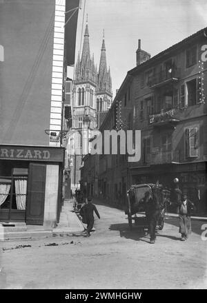 Menschen, die in einer Straße in Voiron der Stadt Chartreuse laufen, trinken in Isère. Mit der Kirche Saint-Bruno im Hintergrund. 20. Jahrhundert. Altes Foto digitalisiert. Stockfoto