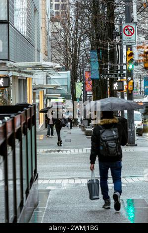 Menschen, die an einem regnerischen Tag auf dem Bürgersteig der Granville Street spazieren gehen und Regenschirme halten. Das grüne Licht der Ampel wird auf dem Gehweg reflektiert. Stockfoto