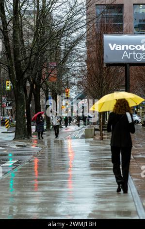 Eine Frau mit einem hellgelben Regenschirm, die an einem regnerischen Tag auf dem Gehweg der Hornby Street neben der Vancouver Art Gallery entlang läuft. Stockfoto