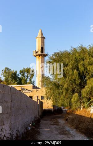 Verlassene Straße von Al Dschazirah Al Hamra spukte die Stadt in Ras Al Khaimah, Vereinigte Arabische Emirate, mit abgerissenen Gebäuden, Zaun und Moschee mit Minarett Stockfoto