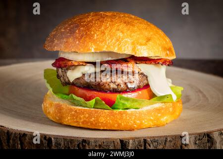 Hausgemachter Cheeseburger mit frischem Salat Tomaten Zwiebeln knuspriger Speck saftiger Rindfleischburger und geschmolzenem Käse in einem Brötchen serviert auf einer Holzplatte aus Naturholz Stockfoto