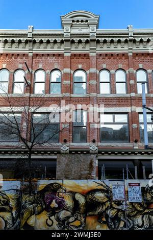 Vancouver, Kanada - 9. Februar 2024: Ein altes Gebäude aus rotem Backstein an der Granville Street, das von Baubarrieren mit bemalten Graffiti-Tieren umgeben ist. Stockfoto