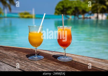 Farbenfrohe Cocktails werden im luxuriösen tropischen Resort-Hotel auf den Malediven serviert. Poolseite mit verschwommenen Palmen und Liegestühlen und Sonnenlicht. Helle, sonnige Farben Stockfoto