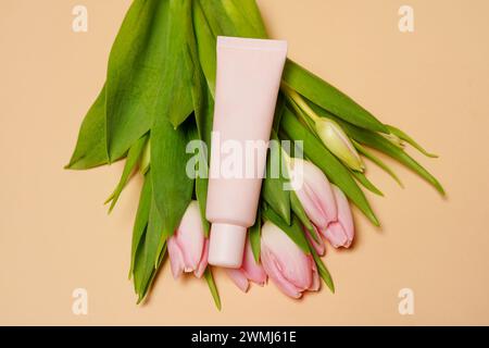 Beige Kosmetikröhre mit Creme oder Lotion für Körper und Strauß von rosa Tulpen auf beigem Hintergrund Stockfoto