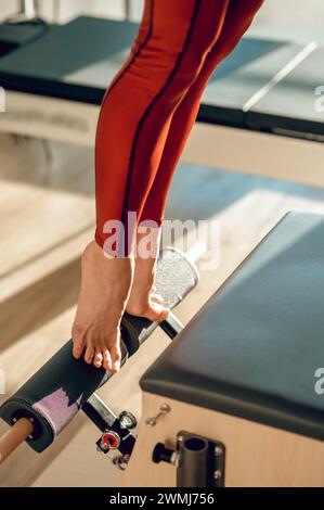 Frau in roten Leggings macht Übungen zur Stärkung der Beinmuskulatur auf Pilates Reformator im Sportstudio Stockfoto