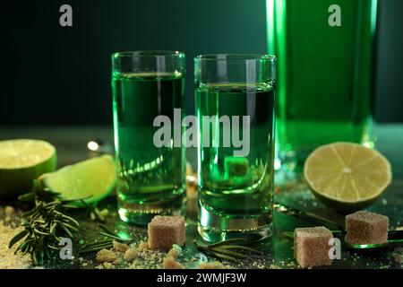 Absinth in Gläsern, brauner Zucker, Limette und Rosmarin auf dem Tisch, Nahaufnahme. Alkoholisches Getränk Stockfoto