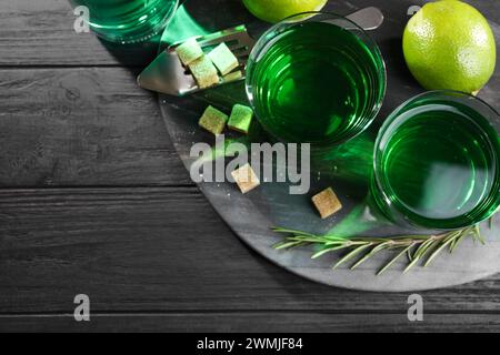 Absinth in Gläsern, Rosmarin, brauner Zucker und Limette auf schwarzem Holztisch, Draufsicht mit Platz für Text. Alkoholisches Getränk Stockfoto