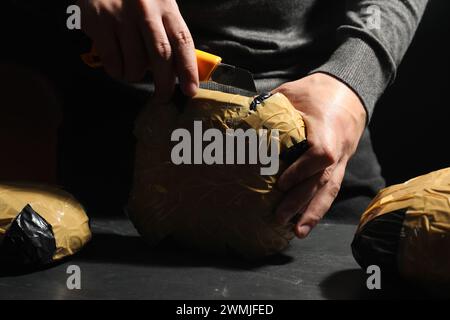 Schmuggel und Drogenhandel. Mann, der ein Paket mit Betäubungsmitteln öffnet, mit einem Koffer in der Dunkelheit, Nahaufnahme Stockfoto