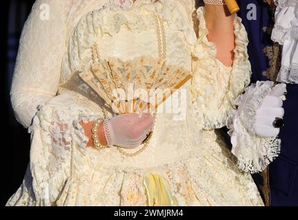 Edelfrau mit luxuriösem, elfenbeinfarbenem historischem Kleid und einem Fan in Handschuhen während der Maskerade-Party in Venedig Stockfoto