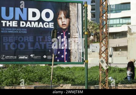 Beirut, Libanon. Februar 2024. Syrische Mutter und Kind stehen am 26. Februar 2024 unter einem Poster der Sensibilisierung für syrische Flüchtlinge in Beirut, Libanon. (Foto: Elisa Gestri/SIPA USA) Credit: SIPA USA/Alamy Live News Stockfoto