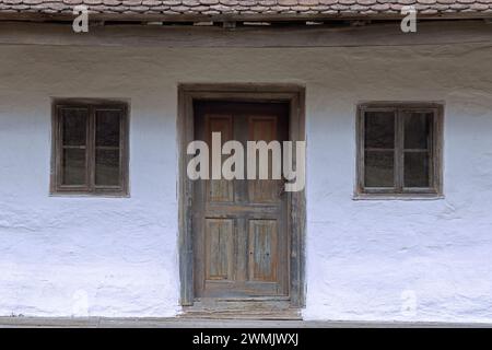 Fassade eines alten rumänischen traditionellen Hauses mit Holztür und zwei kleinen Fenstern Stockfoto
