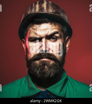 Ernster Industriearbeiter in Uniform und Schutzhelm. Bärtiger Mann mit schmutzigem Gesicht im Schutzhelm. Beruf, Bauwesen, Bauwesen. Schwer Stockfoto