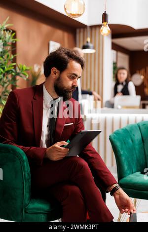 Angestellte, die Dateien auf dem Tablet überprüfen, arbeiten, während er auf den Check-in-Prozess im Hotel wartet. Geschäftsmann liest sich Notizen, bevor er an wichtigen Besprechungen oder Geschäftsreisen teilnimmt. Stockfoto